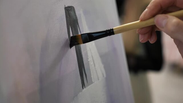 An unknown artist makes brushstrokes against a light background. A creative person with a brush works on a painting in an art studio.