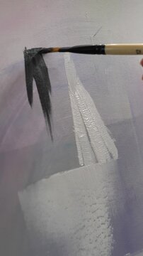 An unknown artist makes brushstrokes against a light background. A creative person with a brush works on a painting in an art studio.