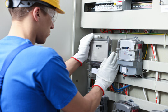 Electrician checking fuse box with electrical meters indoors