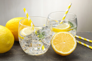 Fototapeta premium Refreshing water in glasses with lemons and rosemary on grey textured table, closeup