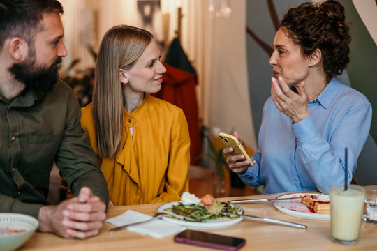 Friends socializing and conversing at restaurant with smartphone