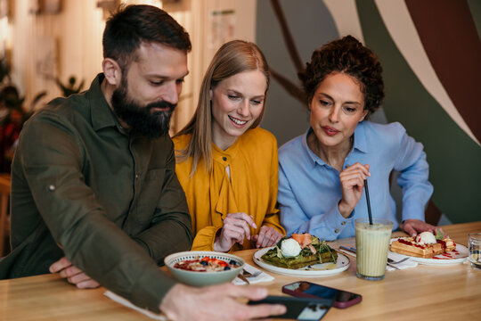 Friends sharing smartphone while enjoying brunch in cafe