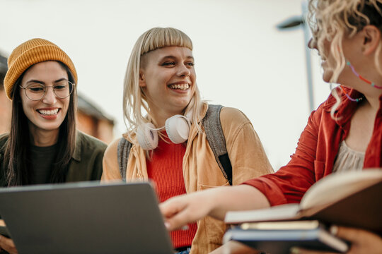 Diverse students learning together outdoors using laptop