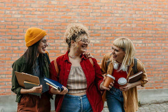 Young women students walking campus together laughing