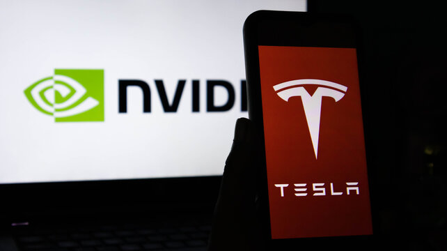 Hand holding a smartphone with the tesla logo in front of a laptop screen displaying the nvidia logo, representing two major technology and ai companies