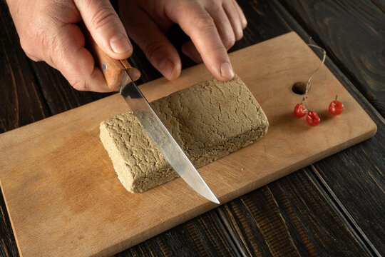 A person uses a knife to cut a block of paste on a wooden board. Red berries sit next to the paste. The scene takes place in a kitchen during the day