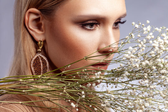 Young woman profile with golden makeup and dried flowers looking aside isolated over gray background
