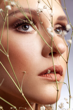 Extreme close up of woman face with professional makeup and long lashes looking through dried flowers isolated over gray background