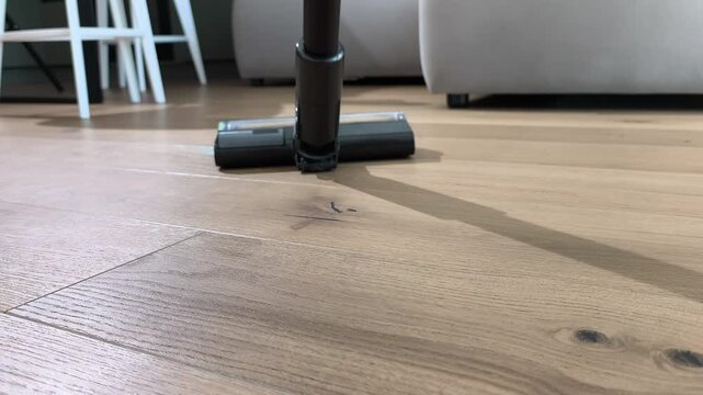 Upright vacuum cleaner moves across wooden floor during cleaning process. Device removes dust using strong suction and rotating brush. Home routine ensures cleanliness and organized interior