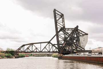 Obraz premium Industrial steel lift bridge over river under dramatic cloudy sky.