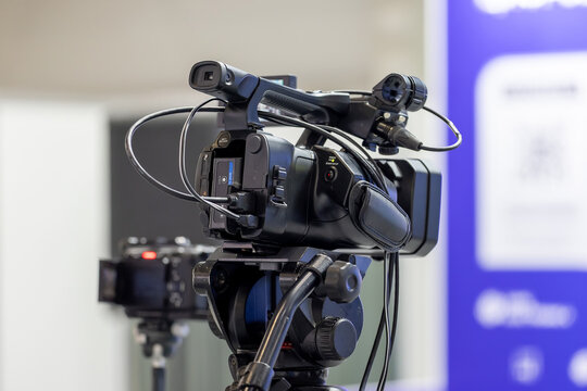 Professional video camera on a tripod recording a business conference event in a modern hall. High quality broadcasting equipment for live streaming and media coverage