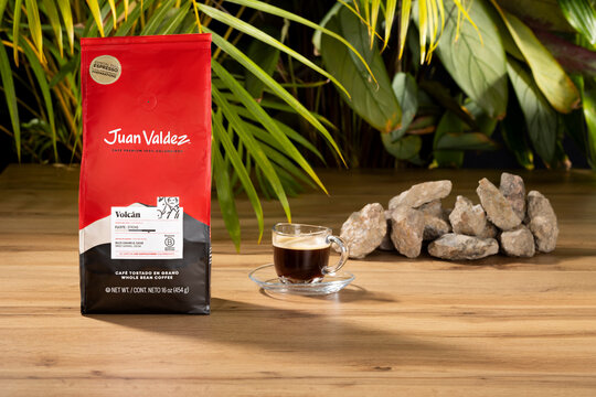 Juan Valdez Volc&aacute;n Colombian whole bean coffee displayed with espresso cup and volcanic stones in tropical studio composition.