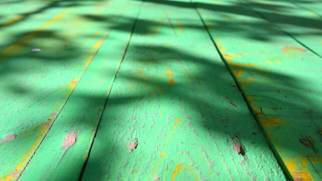 Green wooden planks with tree shadows moving across. Weathered surface with yellow paint patches