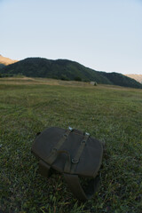Naklejka premium Brown leather bag lying on green grass in open field with hills and clear sky in background natural outdoor scene peaceful environment