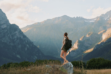 Hiking woman with backpack stands on a rock in a mountain landscape, enjoying nature and solitude, outdoor adventure mood, bright sky. warm sunlight, distant peaks, peaceful © SHOTPRIME STUDIO