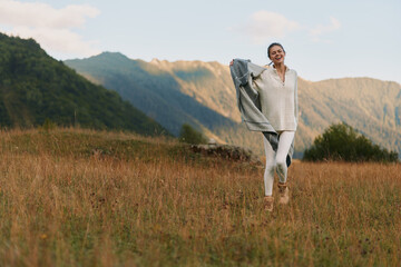 Naklejka premium Joyful woman outdoors in a sunlit field, wearing casual white outfit, breeze lifting her hair, mountains in the background, relaxed lifestyle moment, natural colors and gentle breeze in air