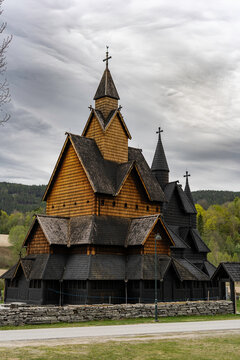 Traditional Norwegian stave church surrounded by spring countryside and forested hills under dramatic cloudy sky in Telemark, Norway. Dark wooden medieval-style architecture. 