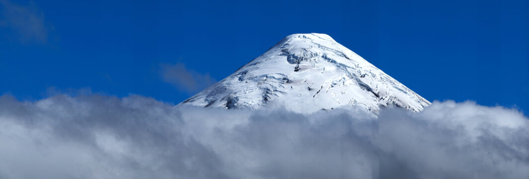 Schneebedeckter Gipfel vom Vulkan Osorno in Chile mit sichtbaren Gletscherspalten &uuml;ber den Wolken vor strahlend blauem Himmel im Sommer Panorama
