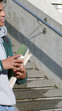 Vertical video: Hearing peer, man in green jacket smiling, holding cup, books on steps, copy space