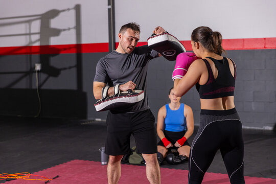 Coach in sportswear holding focus mitts and trainee punching with bright pink gloves on red mat