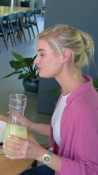 Vertical video: While talking woman in cardigan lifting carafe and moving bowl at table, copy space