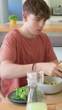 Vertical video: Reaching for bowl teen rust tee adding into bowl tasting pasta to test in kitchen
