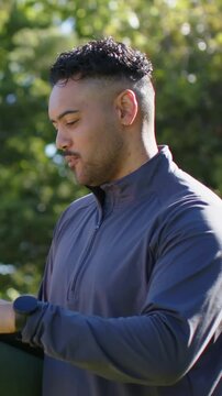 Vertical video: Grabbing man in pullover in park after cue holding mat, checking watch, copy space