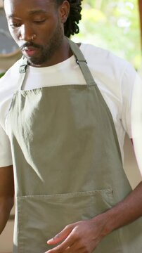 Vertical video: Tapping sieve, man wearing green apron preparing food at kitchen counter with bowl