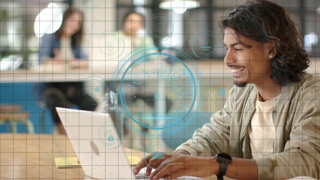 Man typing at table in tech coworking area typing initiating blue HUD overlay showing laptop data