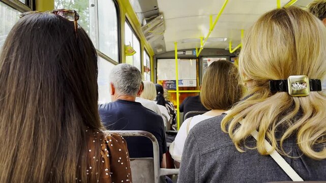 Vintage tram riding with passengers along urban streets. The sunlight highlights the interior and people, capturing the atmosphere of a busy urban commute and the daily rhythm of city life. Slow mo