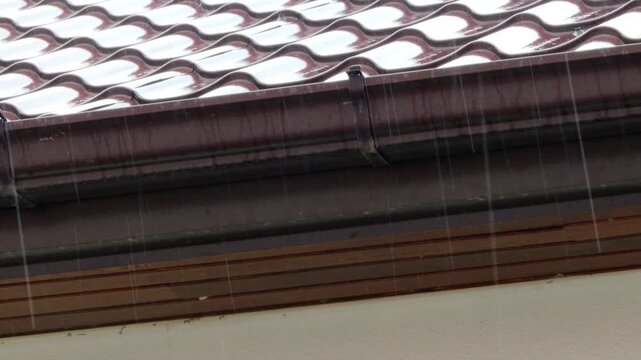 Heavy rain falling on brown roof tiles