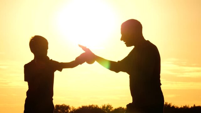 Silhouette of father and son boxing at sunset. Powerful moment of strength, resilience and determination. Outdoor scene symbolizing motivation, growth and inner power in warm light. Fitness family