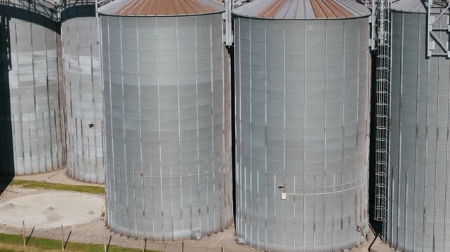Large grain silos are arranged in a row at an agricultural storage facility under clear skies during daylight.