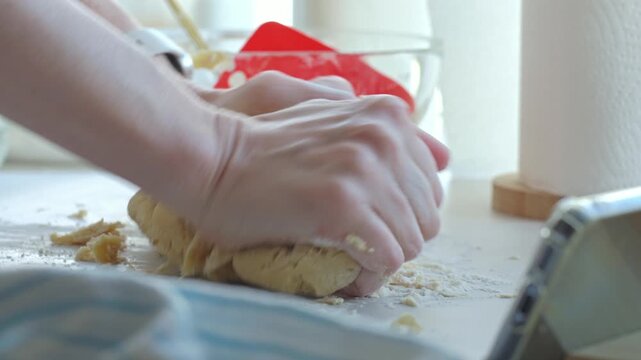 Hands knead dough on floured kitchen counter with baking tools nearby