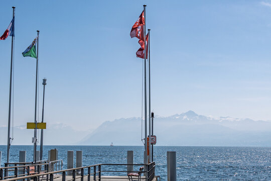 Drapeaux suisses et vaudois flottant sur le quai de Saint-Prex face au lac L&eacute;man et aux Alpes, Suisse