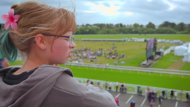 A girl looks from the grandstand of a hippodrome at the crowd of spectators waiting for the horse race. Good mood. Day off. Fun leisure outdoor event