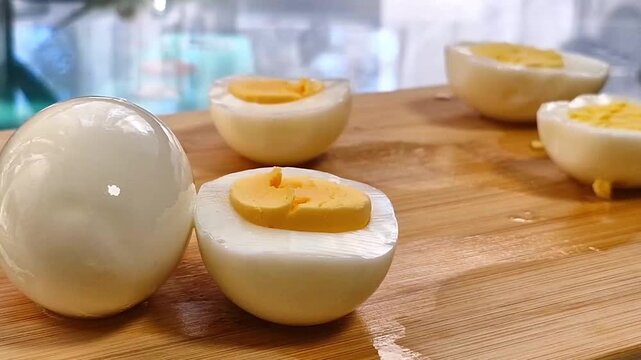 Perfectly peeled boiled eggs with smooth white surface and bright yellow yolk halves resting on wooden cutting board