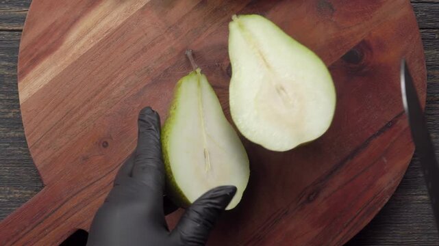 Knife slicing fresh pear in half on wooden board. Top view of cutting fruit for phyllo dough pie. Kitchen baking preparation with ingredients