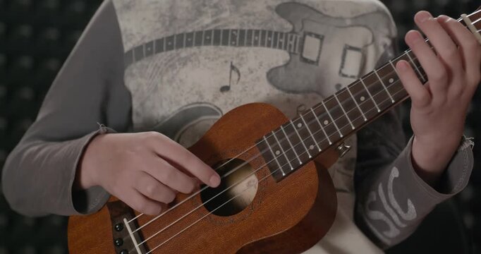 Boy Play Music on Ukulele Instrument in Home Studio. 4K 10-bit