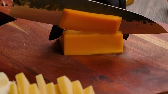 knife slicing cheddar cheese on wooden board with ingredients. Cooking process of making filo pastry pie. Fresh orange dairy preparation in kitchen
