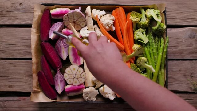 Female hand pouring olive oil on sliced vegetables. Top view panorama of preparing healthy Sunday roast dinner on a baking tray