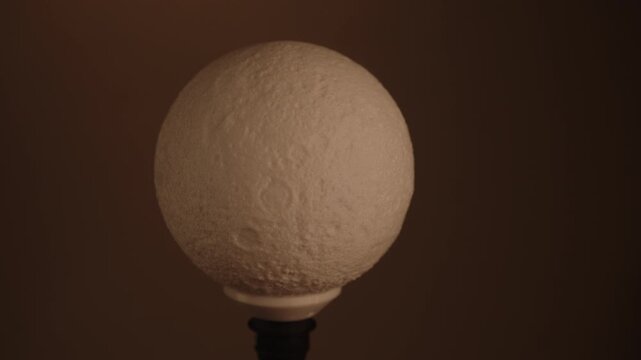 Adjusting brightness of moon shaped night light lamp with dimmer switch, creating relaxing and cozy atmosphere in dark room at home, close-up, nobody. Shooting in slow motion.