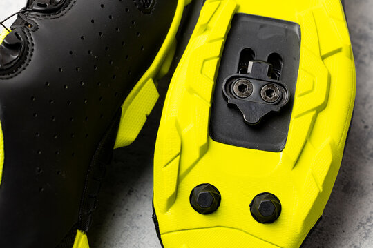 Yellow soles of brand new SPD cycling shoes on gray background. Mountain bike cycling shoes shot with flash light.