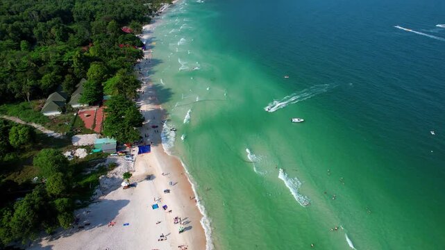Aerial video of the amazing emerald water white sand Sao Beach with lively water sports, tourists, cabanas and sun umbrellas, beach bar and parasailing. Hot sunny day with long waves on Phu Quoc Islan
