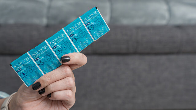 Hand holding Acuvue Oasys 1 Day contact lenses packaging against a blurred gray background, showcasing the brand and product details clearly