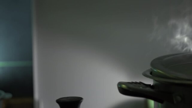 On stove saucepan of boiling liquid sits, steam out from under the lid