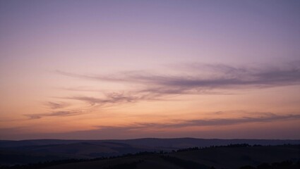 Fototapeta premium Sky displaying layered clouds over rolling hills at sunset