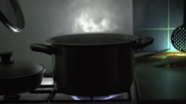 On gas stove human hand lifts the lid from the pot, triggering release of steam