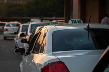 A row of traditional white taxi cars parked at a designated street stand, waiting for passengers.  © AlfRibeiro