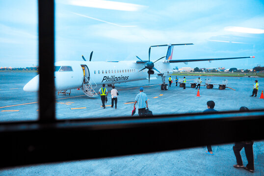 Manila, Philippines: Early morning turboprop airplane flight to Batanes boards at dawn. Crew and passengers on airport tarmac. Shuttle window view.